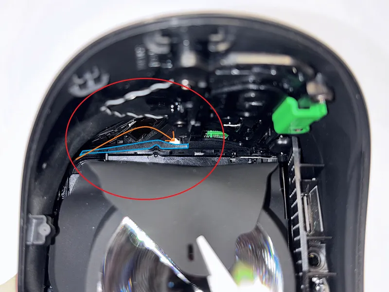 Reference image showing blue-marked plastic piece and orange arrow for cable routing